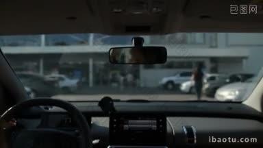 女子驾车驶往购物中心附近的停车场出口，从车辆内部的背景视图显示贸易中心模糊